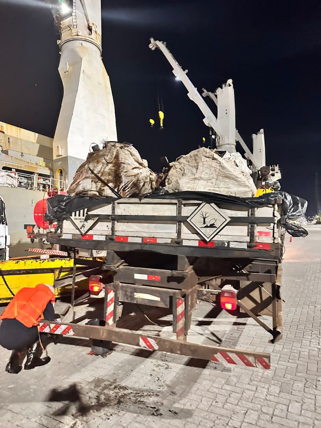 Operação noturna de carregamento de resíduos no porto com guindaste